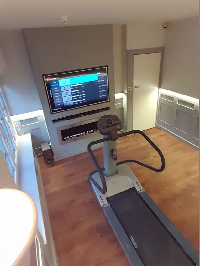 Complete room with TV on the wall and Treadmill after the paneling and LED Tape has been installed